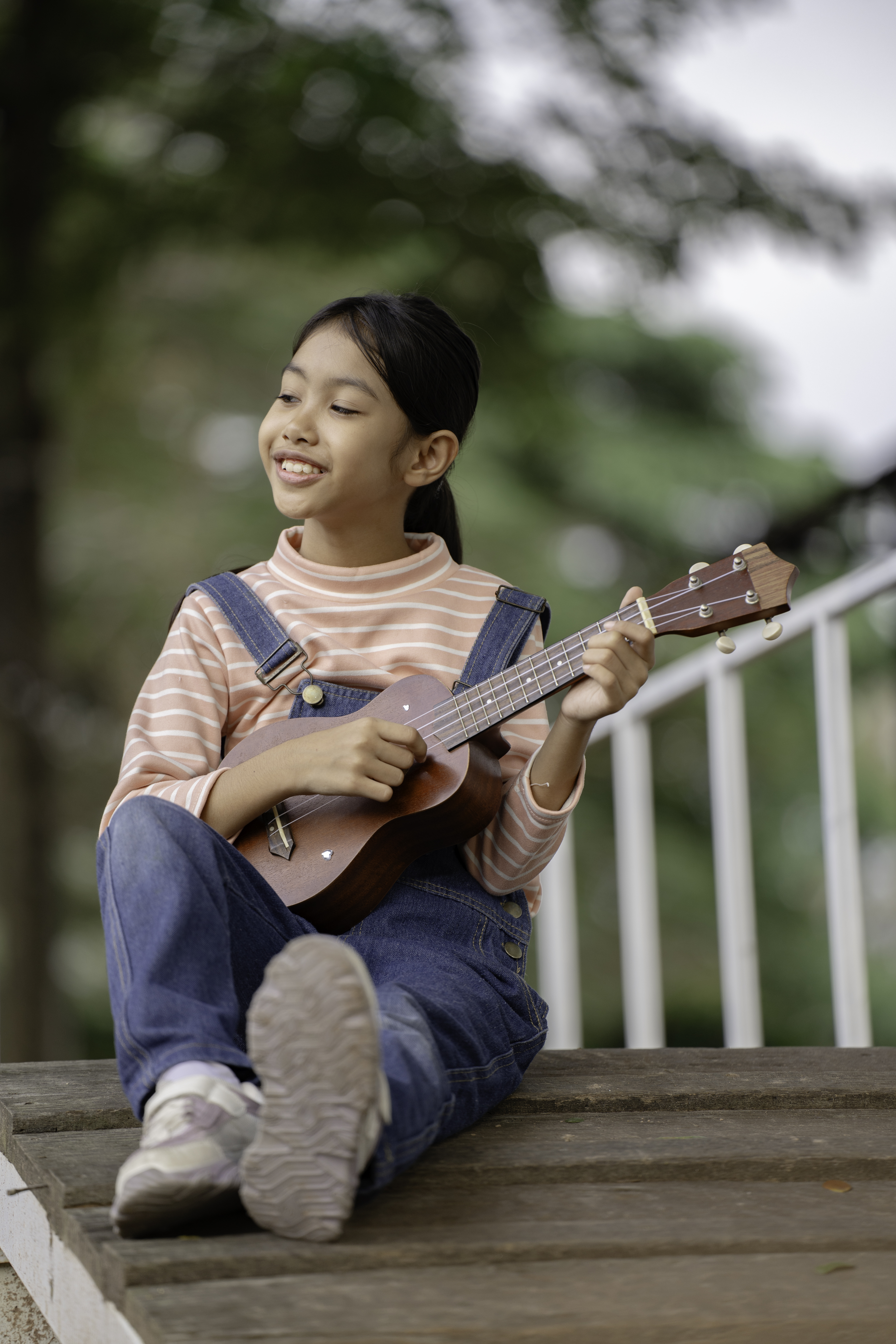 A girl is playing ukulele and singing in the garden.